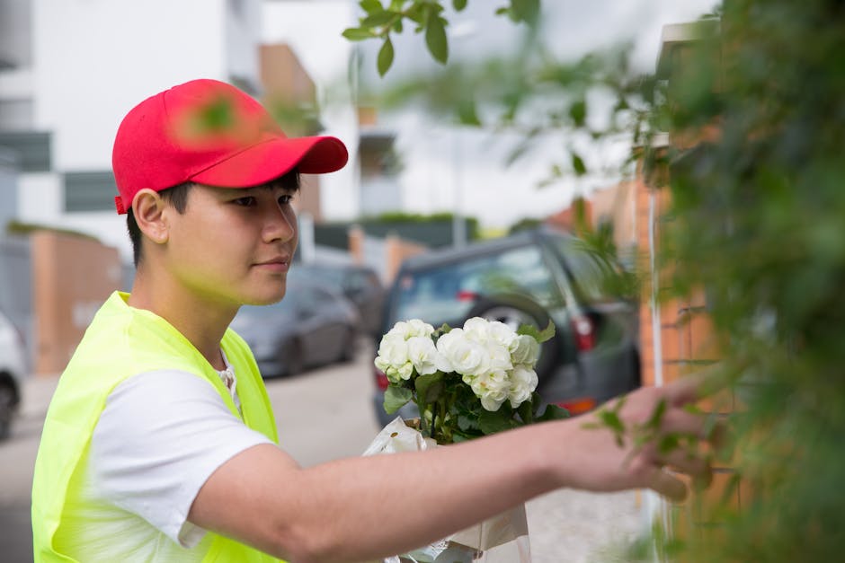 A young woman with light brown hair and bangs, dressed in a beige sweater, holding a large bouquet of fresh flowers close to her face with a gentle, content expression. The bouquet features a variety